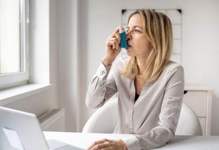 Woman using an asthma inhaler while seated at a desk.