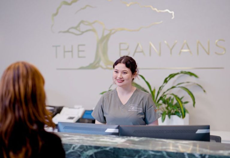 Receptionist speaking with a patient at The Banyans Medical Centre reception desk.