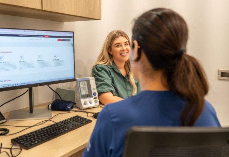 Healthcare professional speaking with a patient during a consultation, with a blood pressure monitor nearby.