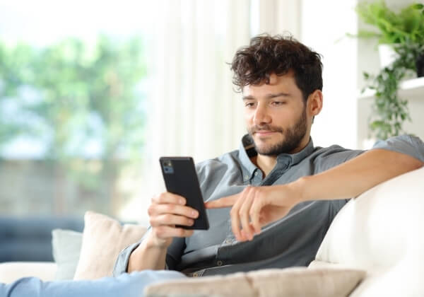 Man using a smartphone while sitting on a sofa at home.