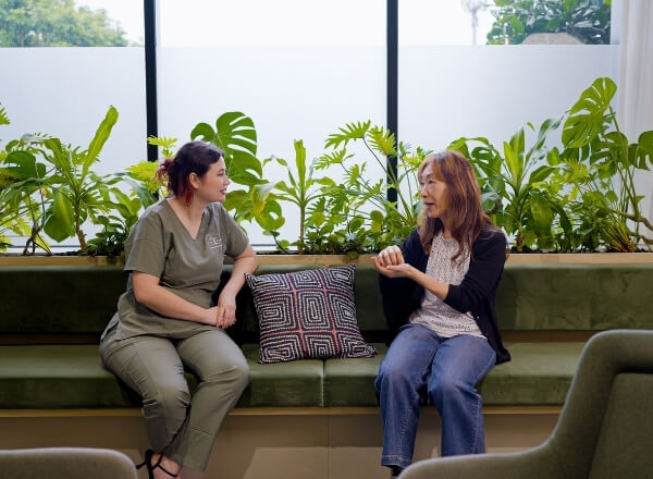 Healthcare practitioner speaking with a patient in a clinic waiting area.